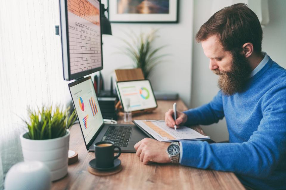 Person looking at graphs on computer and writing a note.